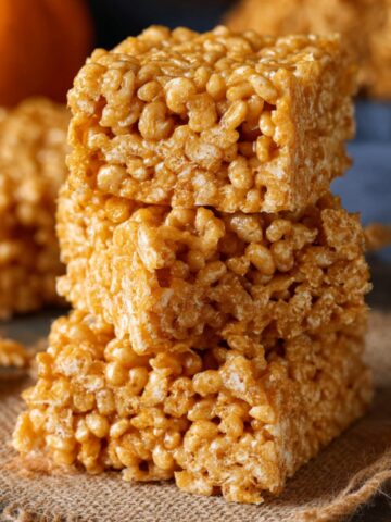 Pumpkin Spice Rice Krispies Recipe 1 A stack of perfectly cut Pumpkin Spice Rice Krispies, showcasing their golden color and crispy texture, set against a warm fall background.