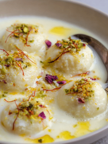 Easy Rasmalai Recipe 3 Rasmalai Recipe soaking in a rich, creamy milk syrup with pistachios and saffron threads sprinkled on top for flavor and color.