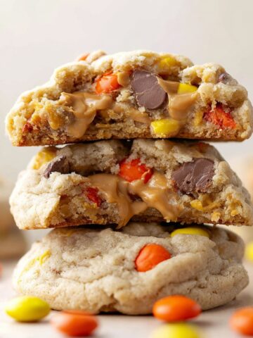 Reese's Pieces Cookies Recipe 3 A stack of gooey Reese's Pieces Cookies, with vibrant orange and yellow candy pieces visible throughout the soft, golden-brown cookies, and a creamy peanut butter center oozing from inside.