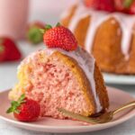 A slice of Strawberry Bundt Cake topped with fresh strawberries and glaze, showing a soft, fluffy pink interior and a light pink glaze.