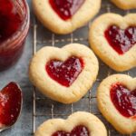 A close-up shot of Thumbprint Jam Cookies filled with strawberry jam on a cooling rack.