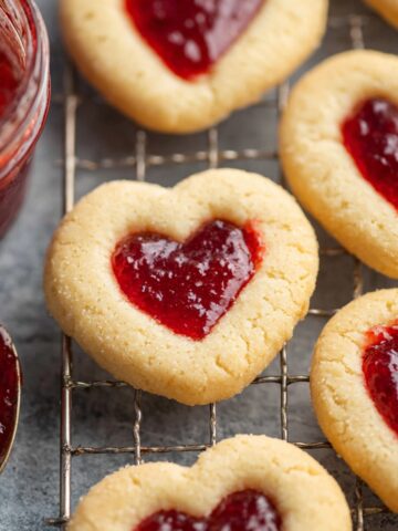 A close-up shot of Thumbprint Jam Cookies filled with strawberry jam on a cooling rack.