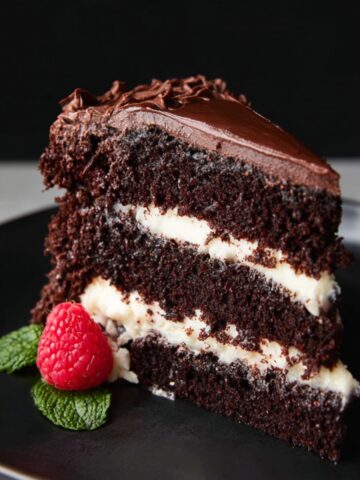 The Best Tuxedo Cake Recipe 1 A decadent slice of Tuxedo Cake, showcasing layers of dark chocolate cake, creamy white filling, and rich chocolate frosting. The cake is garnished with a fresh raspberry and mint leaves.