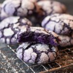Freshly baked Ube Crinkle Cookies with vibrant purple centers and powdered sugar crusts, displaying their signature crinkled texture.