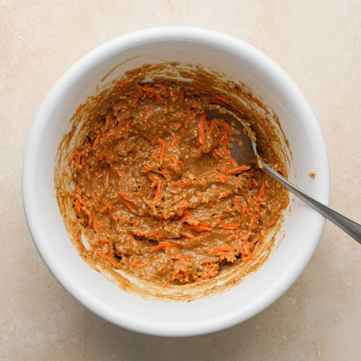 Bowl of carrot cake batter with shredded carrots mixed into the wet mixture, ready to be baked.