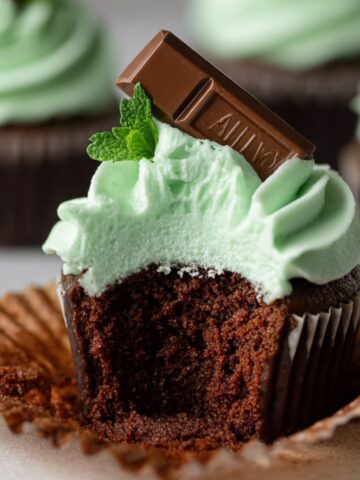 Easy Andes Mint Cupcakes Recipe 2 A freshly baked Andes Mint Cupcakes topped with mint-green frosting and a piece of Andes mint chocolate. A bite has been taken out, revealing the moist chocolate interior.