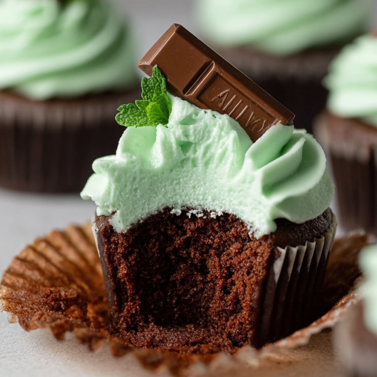 Easy Andes Mint Cupcakes Recipe 9 A freshly baked Andes Mint Cupcakes topped with mint-green frosting and a piece of Andes mint chocolate. A bite has been taken out, revealing the moist chocolate interior.