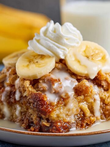 Southern Banana Cobbler Recipe 1 A delicious serving of Banana Cobbler, topped with sliced bananas, whipped cream, and a glaze, with a glass of milk in the background.