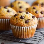 Freshly baked Banana Muffins cooling on a wire rack, with golden brown tops and chocolate chips scattered on top.