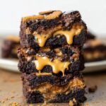 A stack of gooey Biscoff Brownies with a Biscoff cookie crust, featuring a melting peanut butter center spilling out from between the layers.
