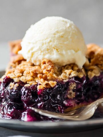 Blueberry Crumble Pie Recipe 2 A slice of Blueberry Crumble Pie served on a plate with a scoop of vanilla ice cream on top, showing the vibrant blueberry filling and golden crumble topping.
