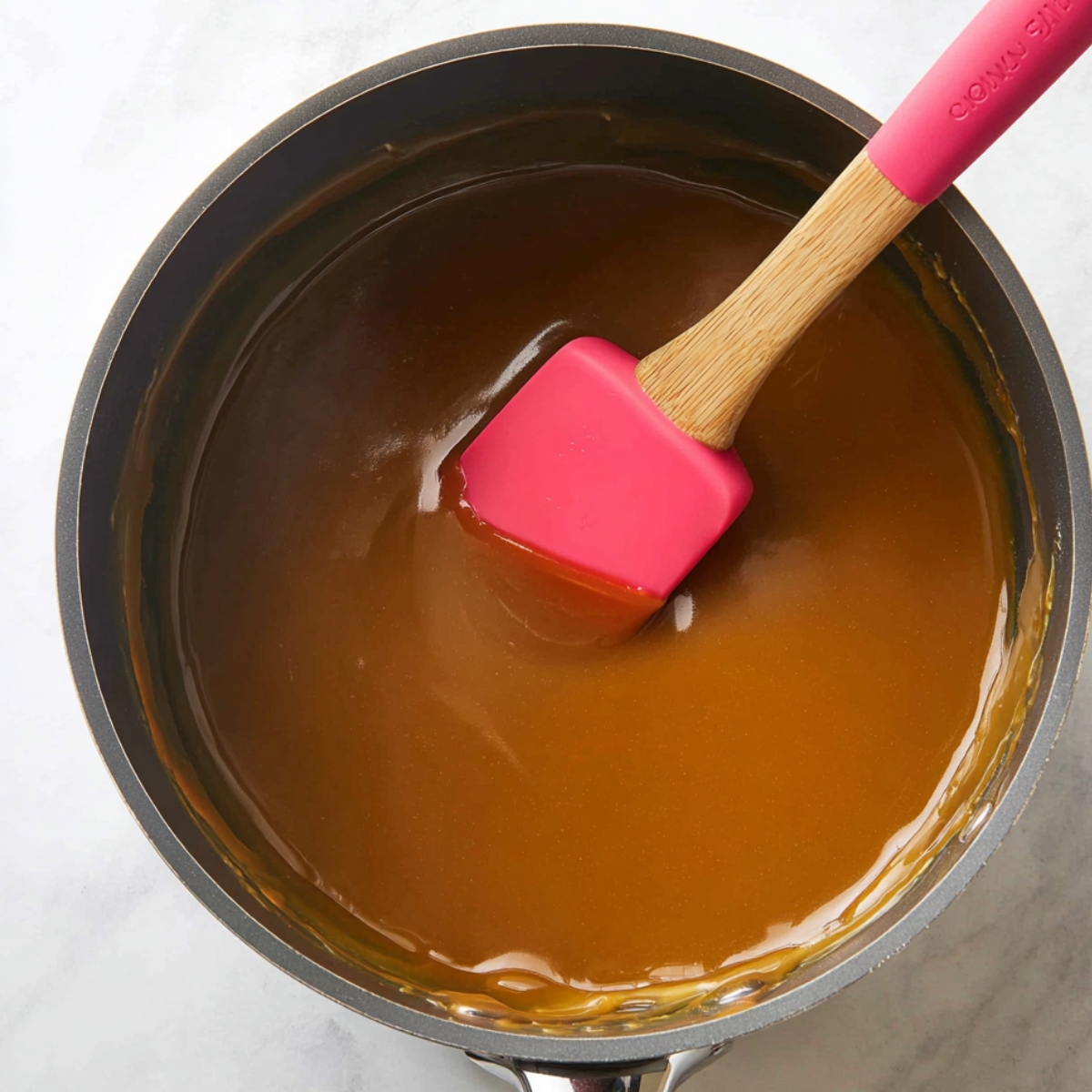 The Best Caramel Turtle Pie Recipe 11 Smooth caramel sauce in a saucepan with a wooden spatula.
