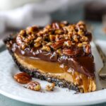 Slice of Caramel Turtle Pie topped with pecans and a glossy layer of chocolate.
