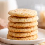 A stack of freshly baked golden Chewy Coconut Sugar Cookies arranged on a plate, showcasing a crisp texture with visible coconut flakes.