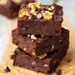 A stack of three Chickpea Brownies with visible walnut pieces and chocolate chips on top, served on parchment paper.