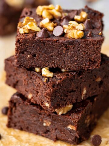 A stack of three Chickpea Brownies with visible walnut pieces and chocolate chips on top, served on parchment paper.