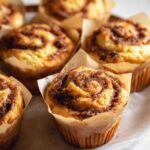 A batch of freshly baked Cinnamon Roll Muffins with a golden brown top, lightly sprinkled with sugar.