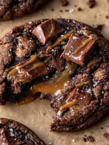 Coffee Toffee Cookies Recipe 4 A gooey, Coffee Toffee Cookies with chunks of chocolate and caramel oozing from the center, with a bite taken out and a sprinkle of sea salt on top.