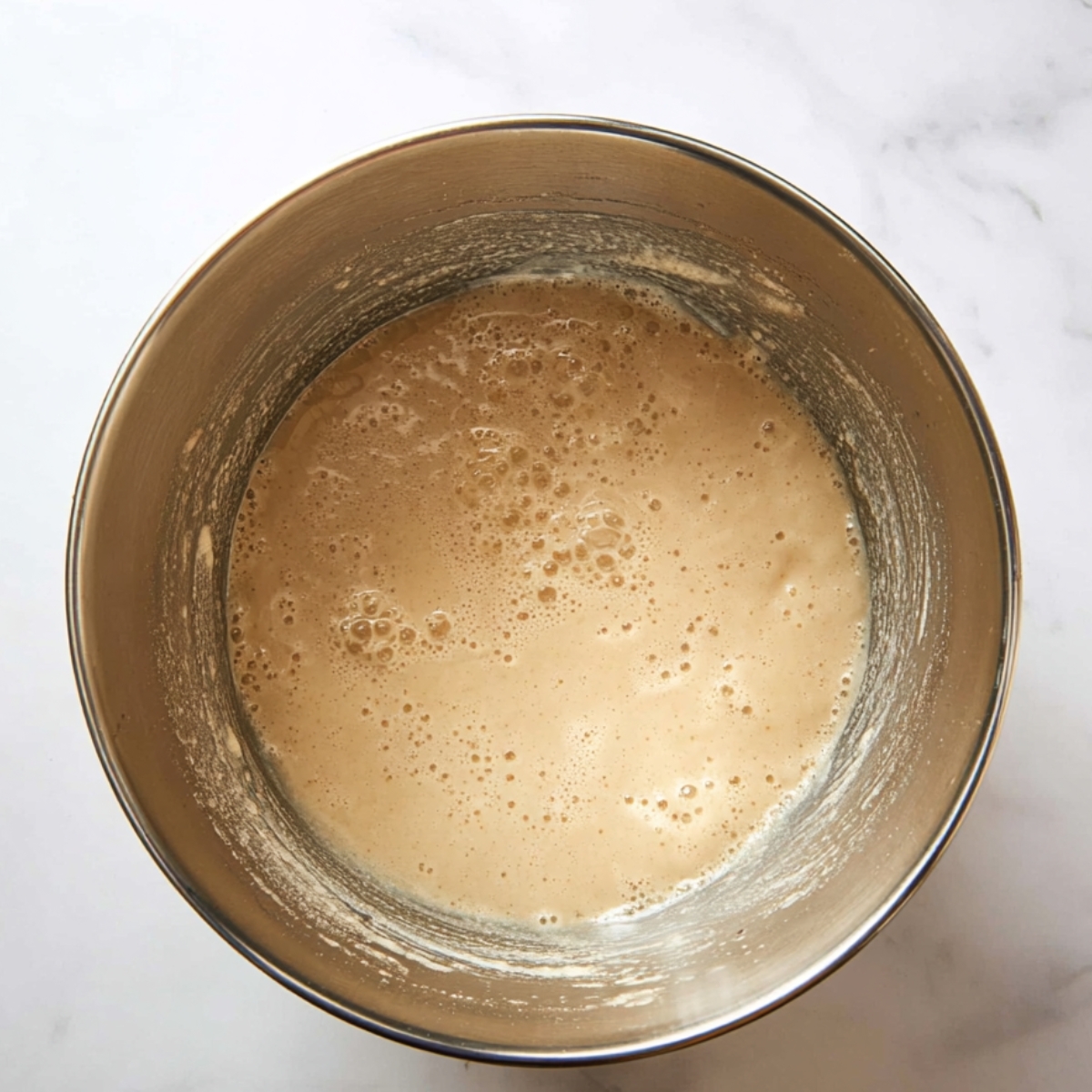 A mixing bowl with a smooth, bubbly beige batter, showing the early stage of preparation for banana pudding cupcakes.