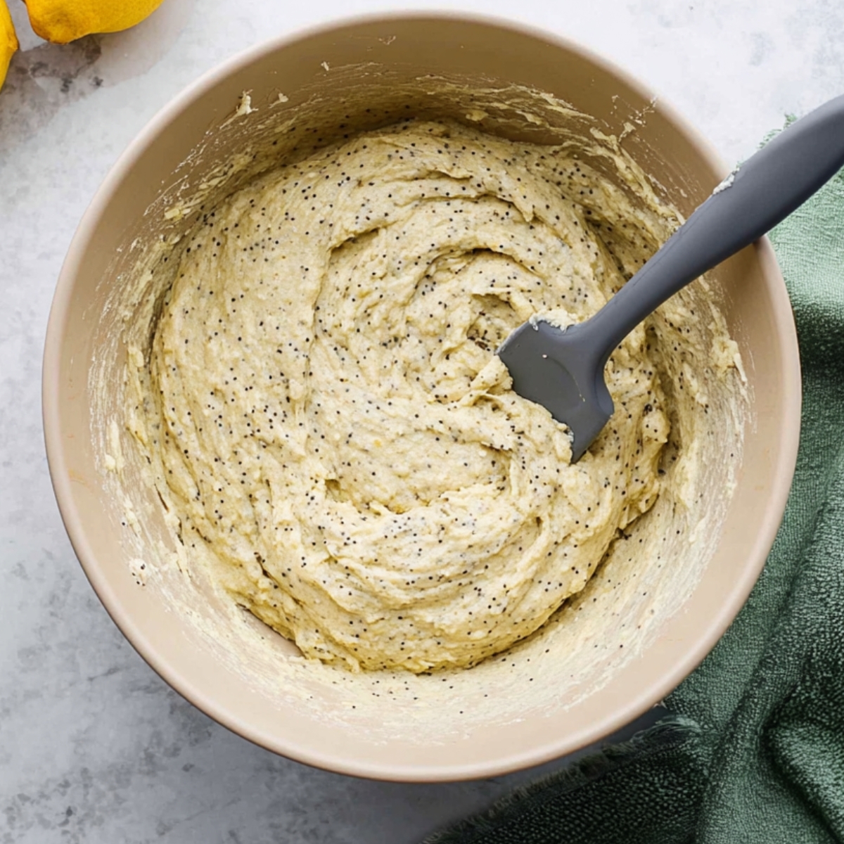 A mixing bowl with wet and dry ingredients for lemon poppy seed cookies being combined, creating a smooth dough.