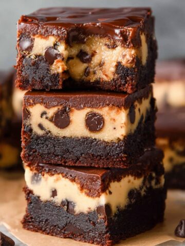 The Best Cookie Dough Brownies Recipe 1 Close-up of stacked Cookie Dough Brownies with chocolate chips, topped with a shiny layer of chocolate ganache.