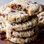 Stack of freshly baked Cranberry Orange Icebox Cookies drizzled with white icing. The cookies have a soft, crumbly texture with visible dried cranberries and a hint of orange zest.