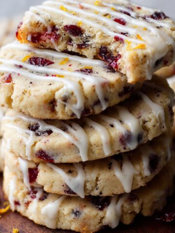 Stack of freshly baked Cranberry Orange Icebox Cookies drizzled with white icing. The cookies have a soft, crumbly texture with visible dried cranberries and a hint of orange zest.