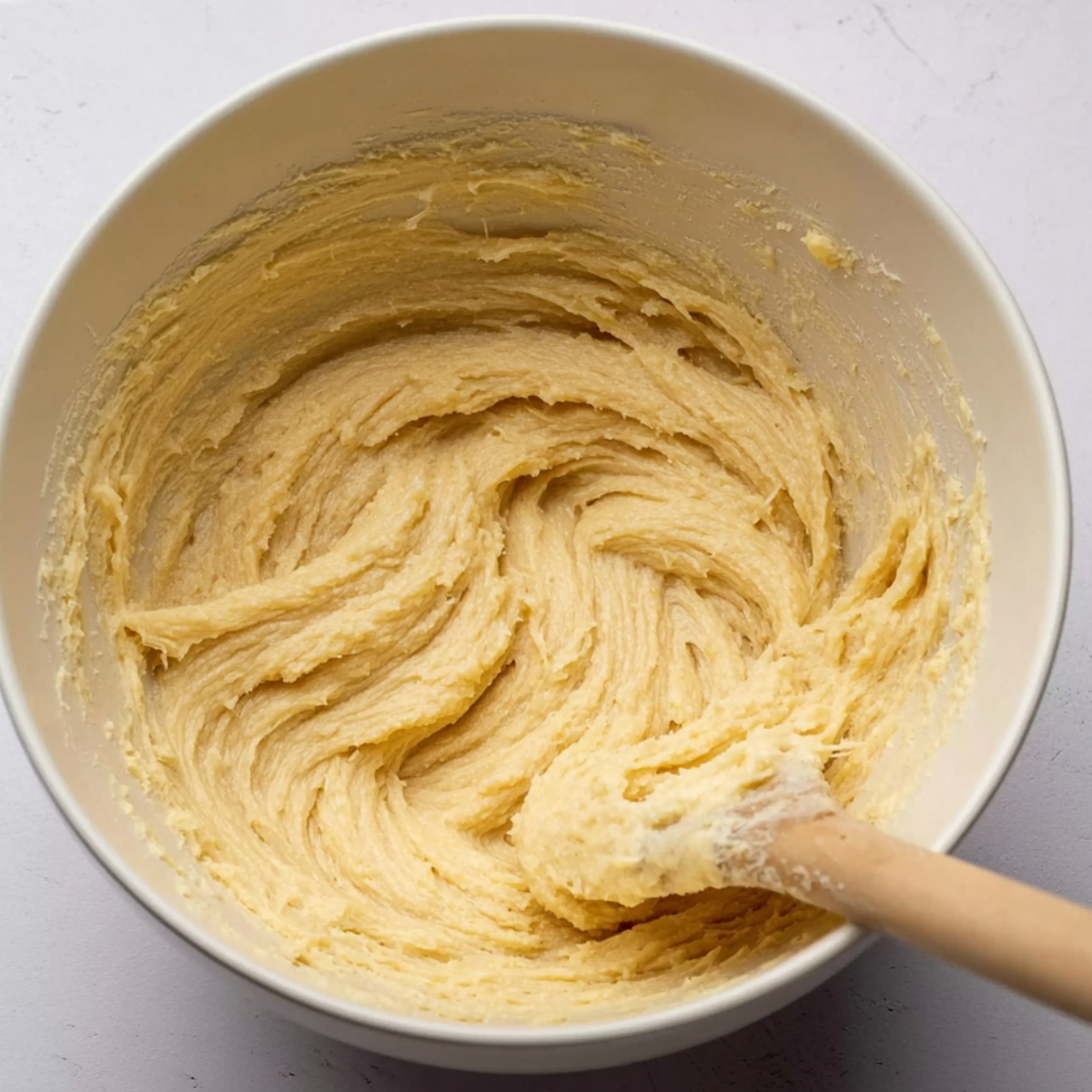 Best Raspberry Almond Cake Recipe 10 A smooth and creamy cake batter in a mixing bowl, showing its fluffy texture, prepared for baking with a wooden spatula.