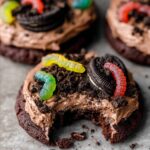 Dirt Cake Cookies topped with creamy chocolate frosting, crumbled Oreo cookies, and gummy worms for a playful dirt cake-inspired look.