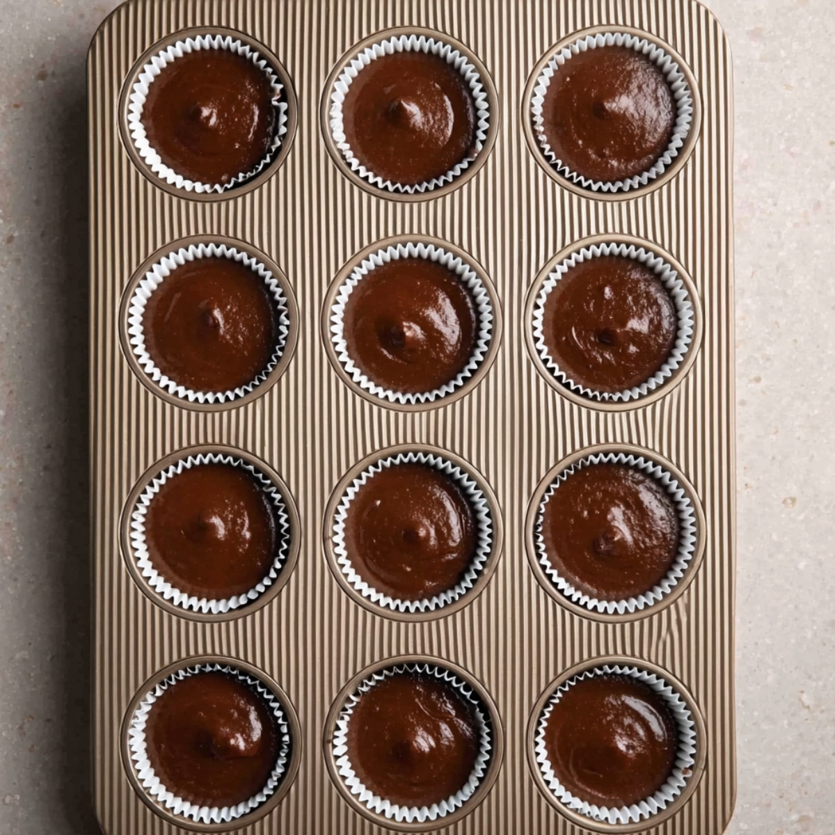 Easy Andes Mint Cupcakes Recipe 11 A muffin tin filled with white cupcake liners, each containing smooth chocolate batter. The batter is evenly distributed, with a glossy finish, ready for baking.