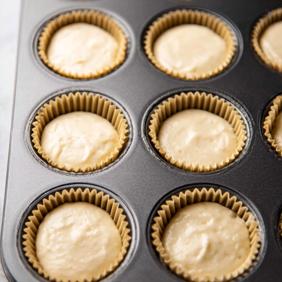 The Best Vanilla Cupcakes Reipe 11 Vanilla cupcake batter evenly poured into cupcake liners, ready to bake into fluffy cupcakes.