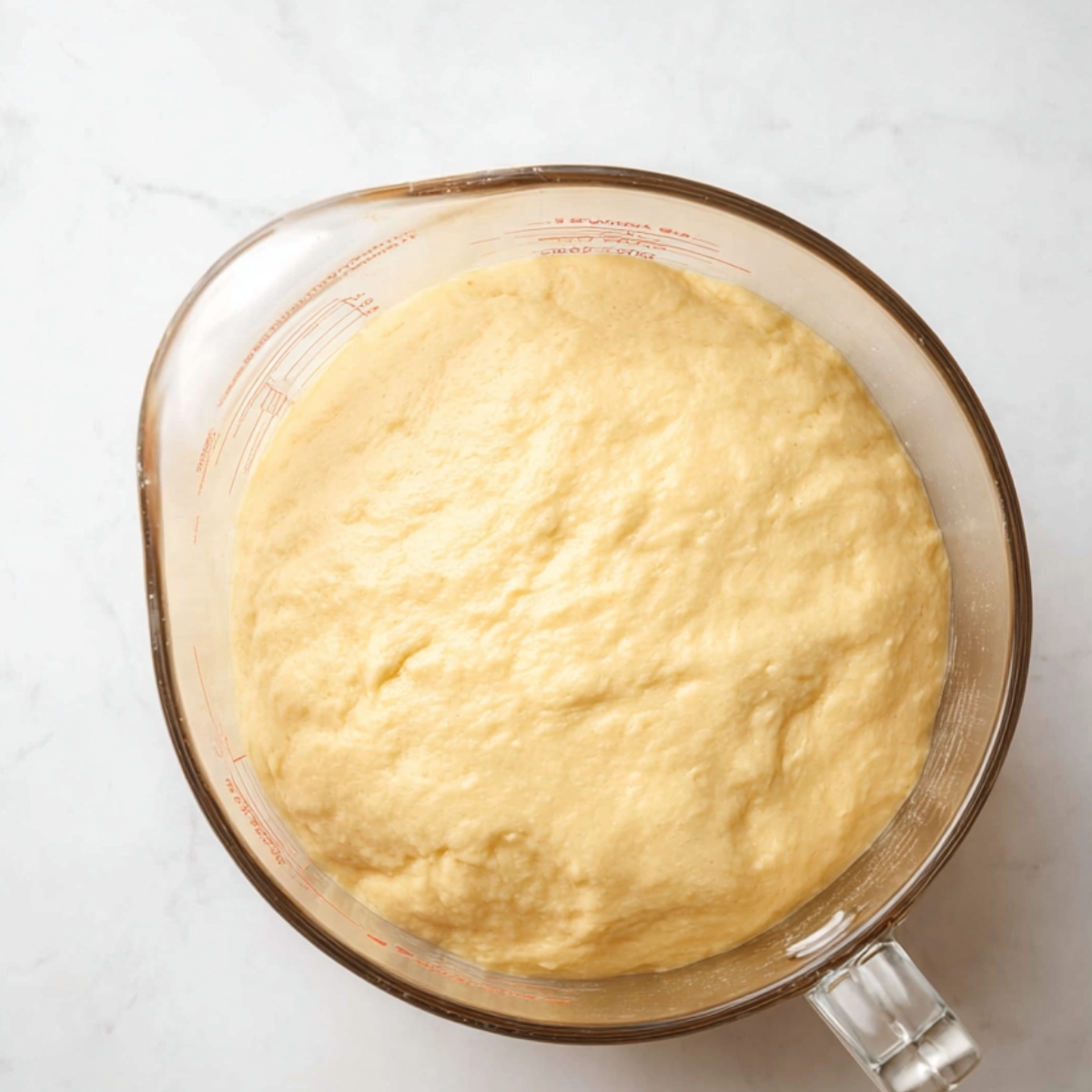 The Best Challah Bread Recipe 11 Glass measuring cup with dough that has risen and expanded, showing a smooth, soft texture, with the dough almost reaching the top of the cup.