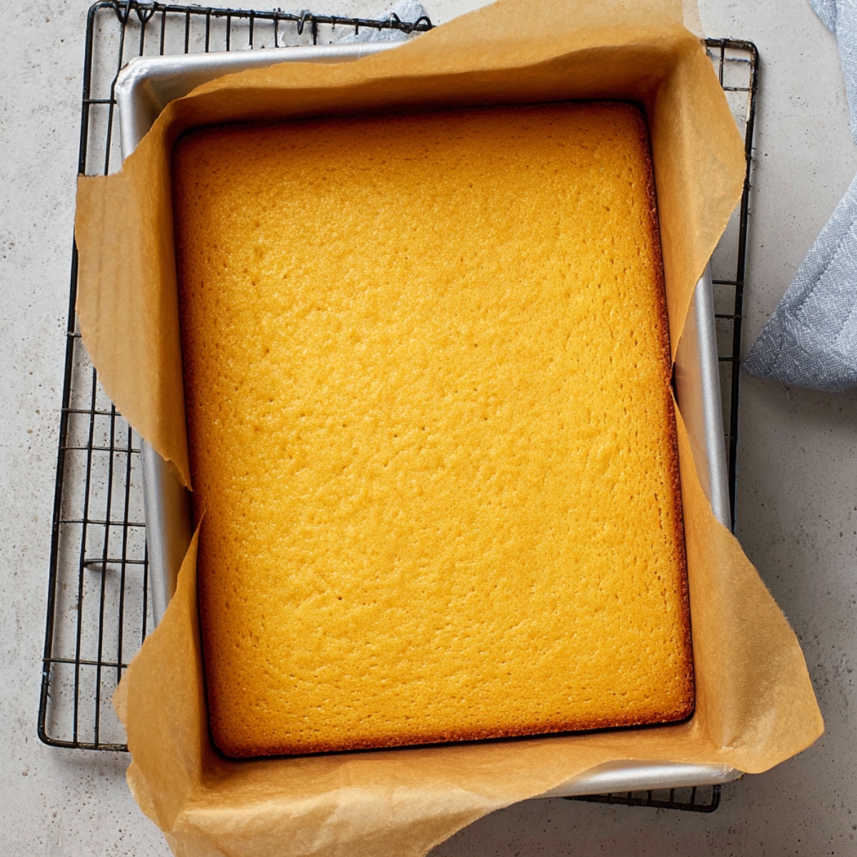 A fresh, golden yellow cake in a baking pan, cooling on a wire rack.