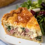 A slice of Italian Easter Pie, showcasing a golden, flaky crust with a savory filling of ham, sausage, ricotta, and spinach, served with a fresh salad on the side.
