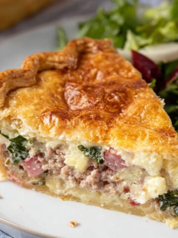 Italian Easter Pie (Pizza Rustica) 3 A slice of Italian Easter Pie, showcasing a golden, flaky crust with a savory filling of ham, sausage, ricotta, and spinach, served with a fresh salad on the side.