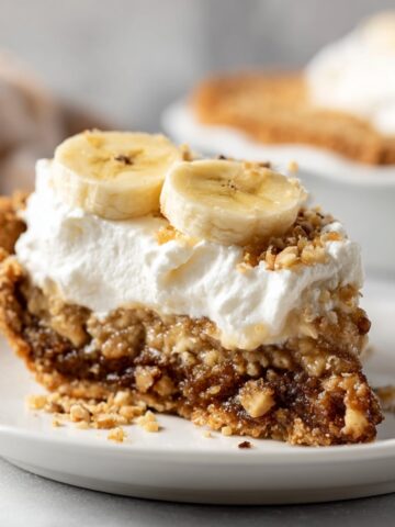 Easy Southern Kentucky Sawdust Pie Recipe 6 A close-up slice of Kentucky Sawdust Pie topped with whipped cream, banana slices, and chopped nuts on a white plate.