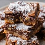 Stack of Knock You Naked Bars with powdered sugar dusted on top, showcasing the layers of caramel, chocolate, and pecans.