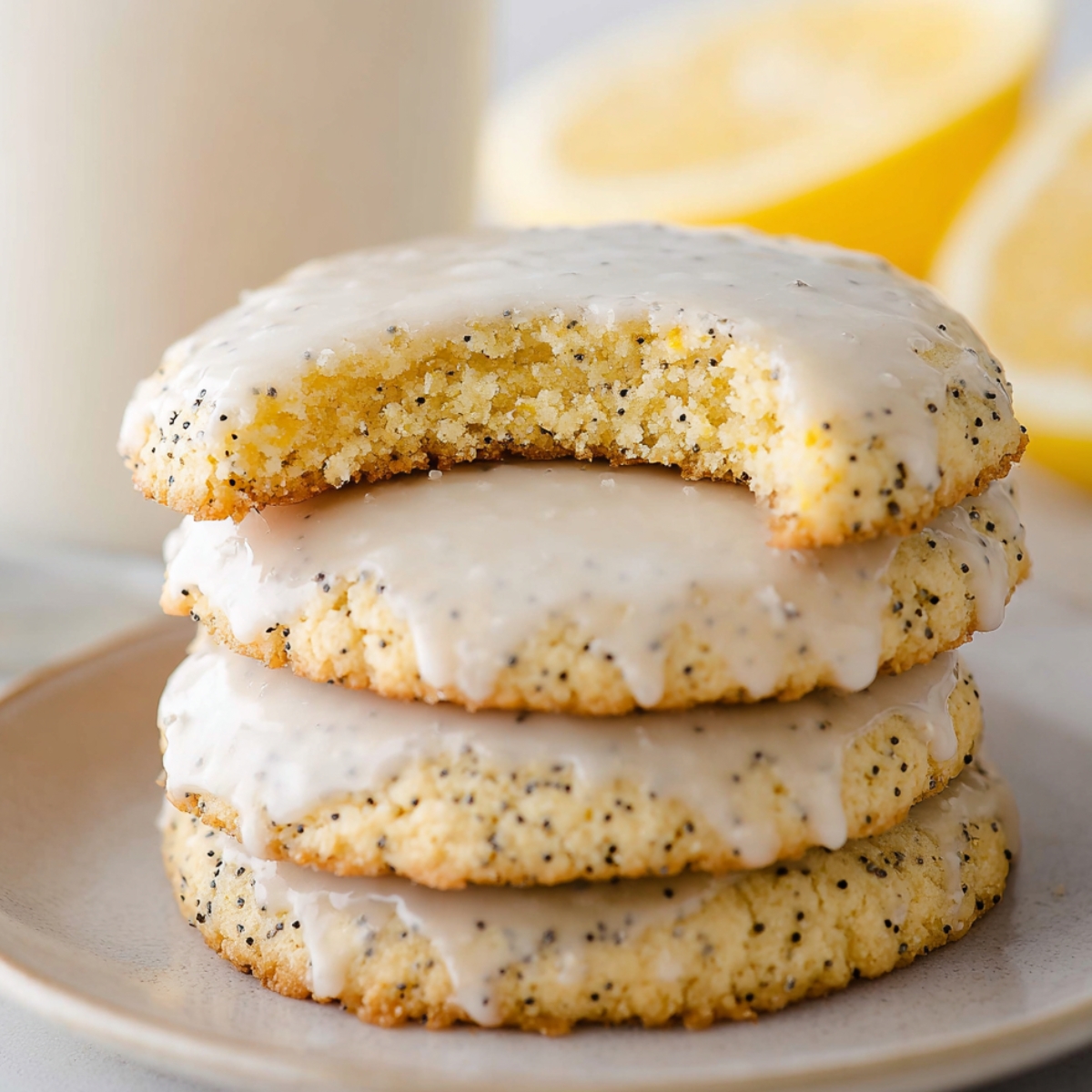 A close-up of stacked, glazed Lemon Poppy Seed Cookies with a bite taken out of the top cookie, showcasing the soft, crumbly texture.