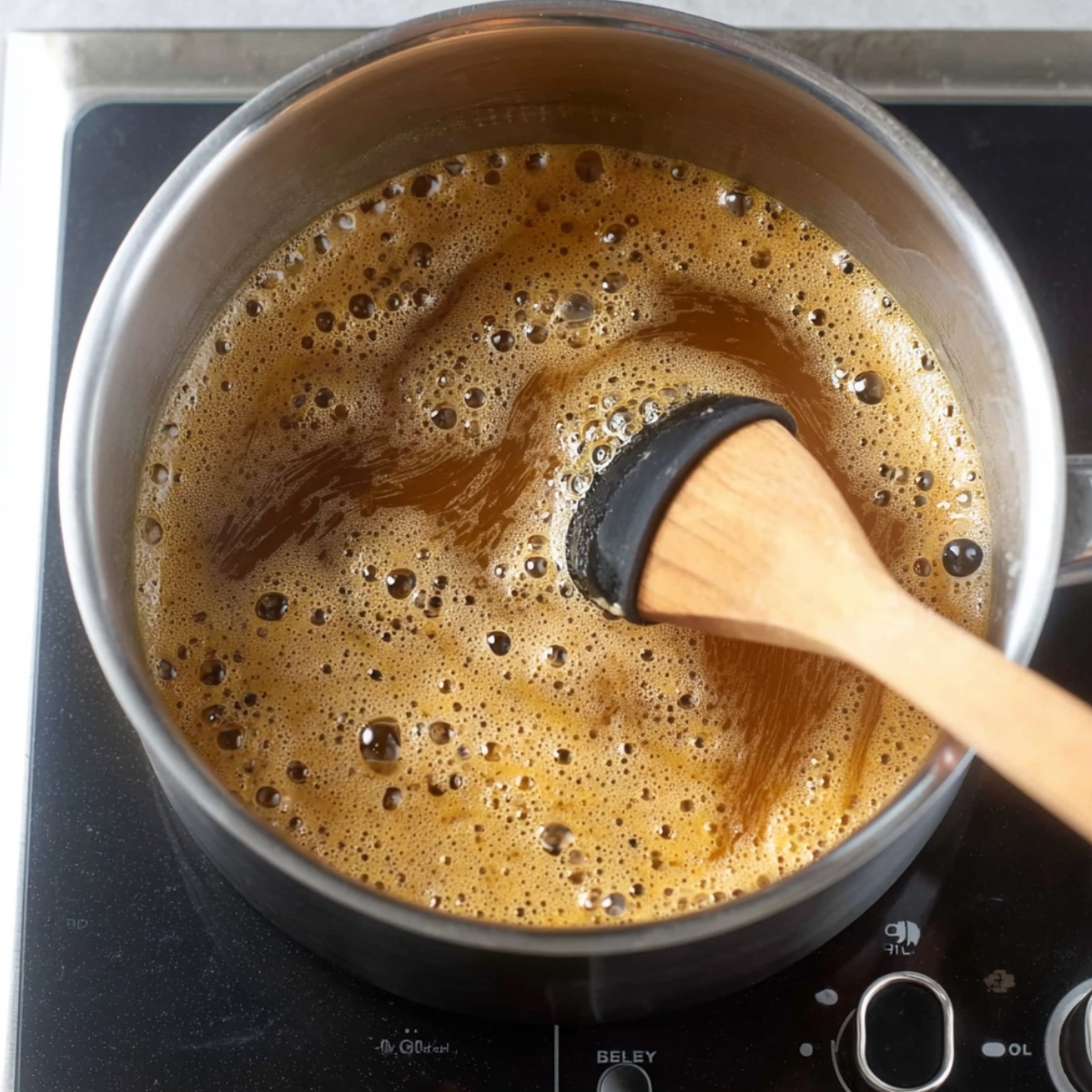 Easy Butterscotch Crunch Cake 11 A saucepan with bubbling butterscotch sauce on a stovetop, being stirred with a wooden spoon.