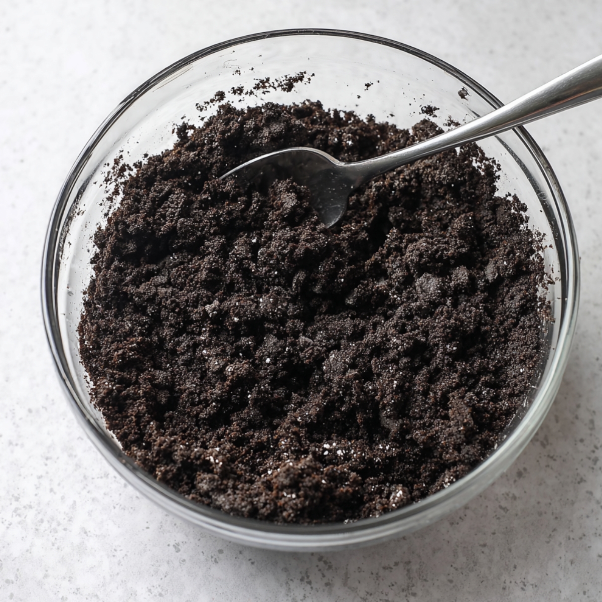 The Best Caramel Turtle Pie Recipe 10 Crumbled chocolate cookies in a glass bowl with a spoon.