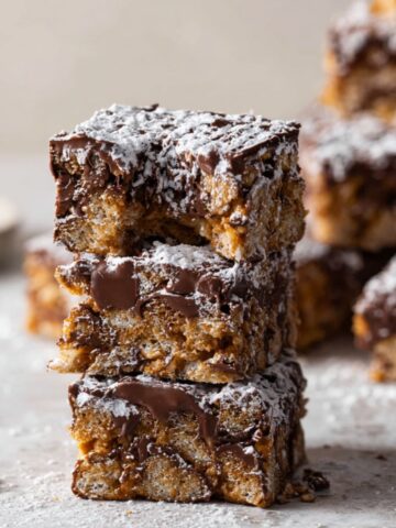 Easy Muddy Buddy Bars Recipe 2 Three stacked muddy buddy bars, dusted with powdered sugar, showcasing the chocolate and cereal layers with a soft, crumbly texture.