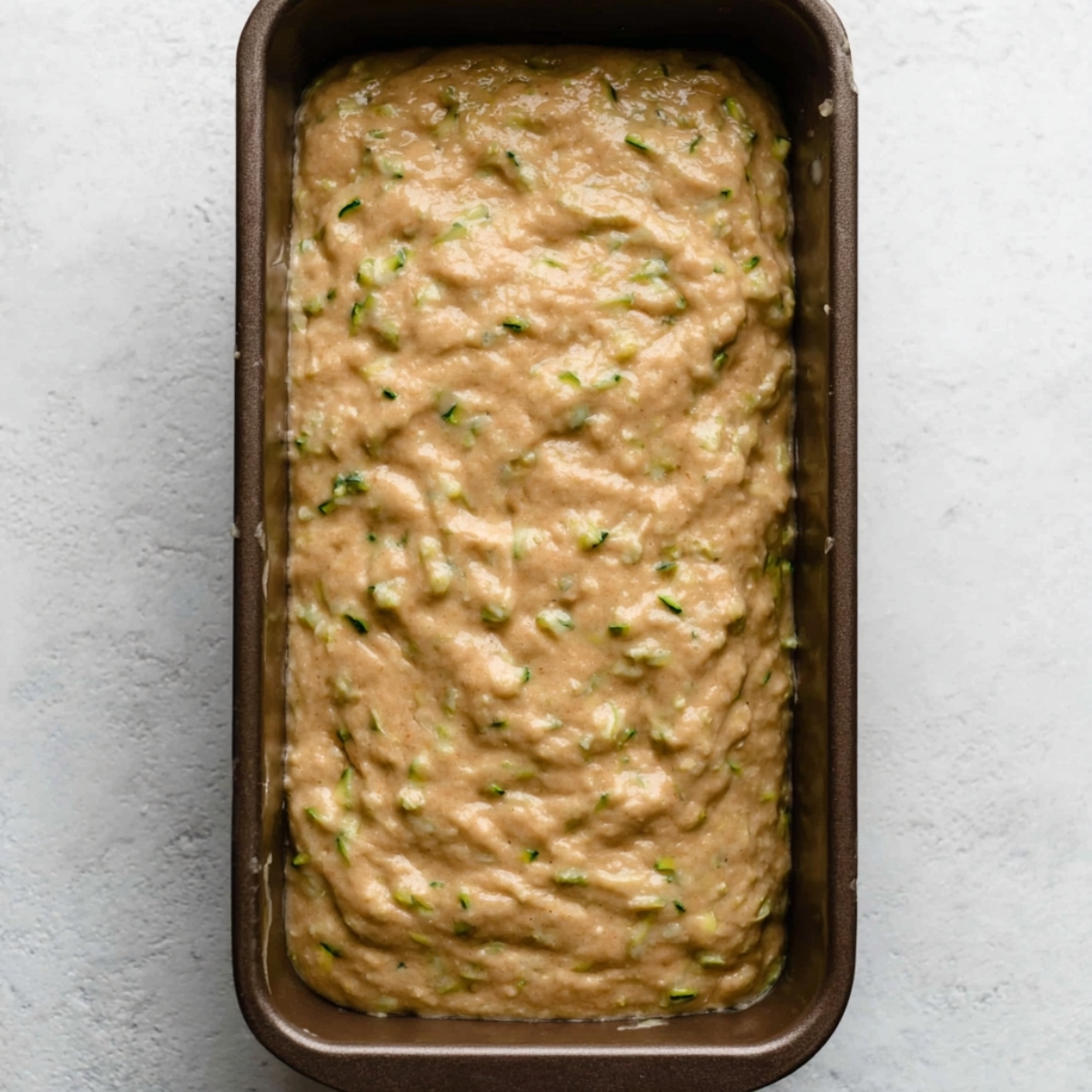 Moist Zucchini Bread Recipe 11 A loaf pan filled with zucchini bread batter, ready to be baked, showing a smooth and thick mixture with visible zucchini pieces.
