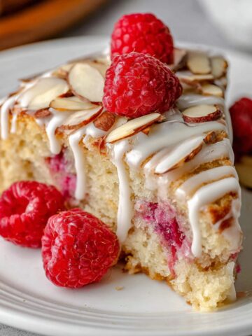 Best Raspberry Almond Cake Recipe 1 A slice of Raspberry Almond Cake drizzled with icing, topped with fresh raspberries and slivered almonds, showcasing a moist interior with vibrant raspberry filling.