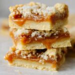 A close-up of stacked Salted Caramel Butter Bars, showcasing the layers of caramel in between the buttery cookie base.