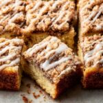 Slices of Sour Cream Coffee Cake topped with a crumbly streusel and drizzled with icing, arranged neatly on parchment paper.