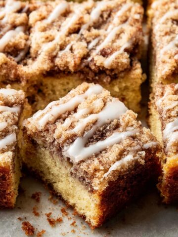 Sour Cream Coffee Cake Recipe 1 Slices of Sour Cream Coffee Cake topped with a crumbly streusel and drizzled with icing, arranged neatly on parchment paper.
