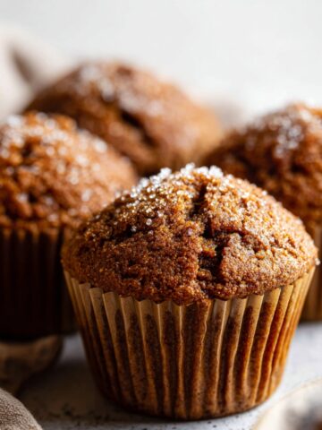 Spiced Molasses Gingerbread Muffins 1 A close-up of freshly baked Spiced Molasses Gingerbread Muffins in paper liners, with a sprinkle of sugar on top, placed on a clean, soft background.