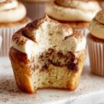 A close-up of a Tiramisu Cupcakes with a bite taken out, revealing the moist interior with a swirl of espresso flavor and topped with creamy mascarpone frosting, dusted with cocoa powder.