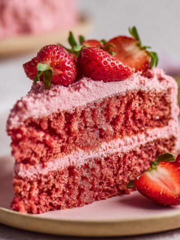 Easy Vegan Strawberry Cake Recipe 4 A close-up of a slice of Vegan Strawberry Cake showing soft, fluffy layers with pink frosting and fresh strawberries on top.