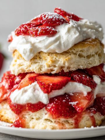 Delicious Vegan Strawberry Shortcakes 2 A stacked Vegan Strawberry Shortcakes, layered with fluffy biscuit, whipped cream, and fresh strawberries, dusted with powdered sugar.